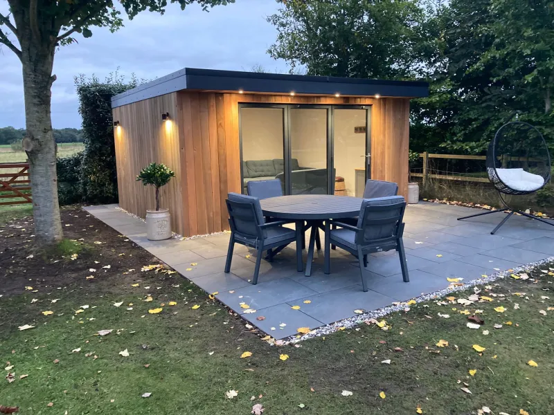 Completed cedar garden room at dusk with outdoor patio and dining by AG Joinery Lancashire