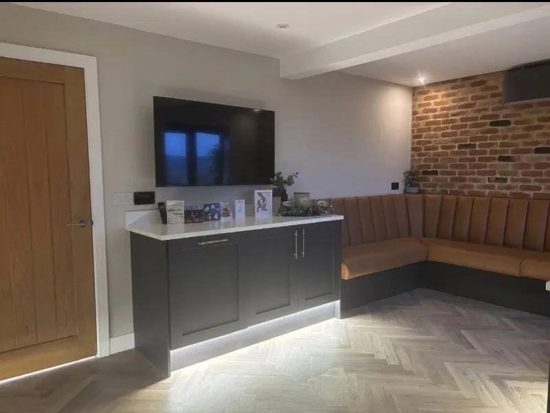 Media wall with herringbone flooring and exposed brick by AG Joinery