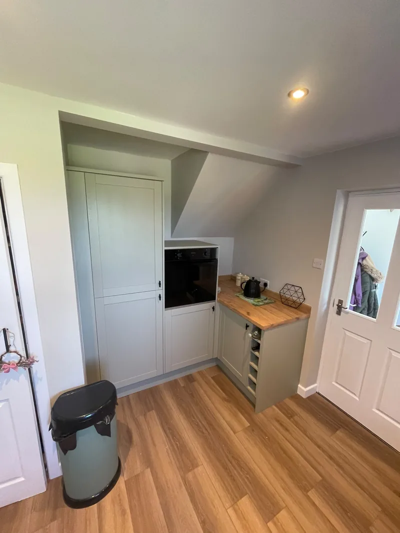 Sage green shaker kitchen with full-height larder unit, built-in oven and oak worktop by AG Joinery Lancashire